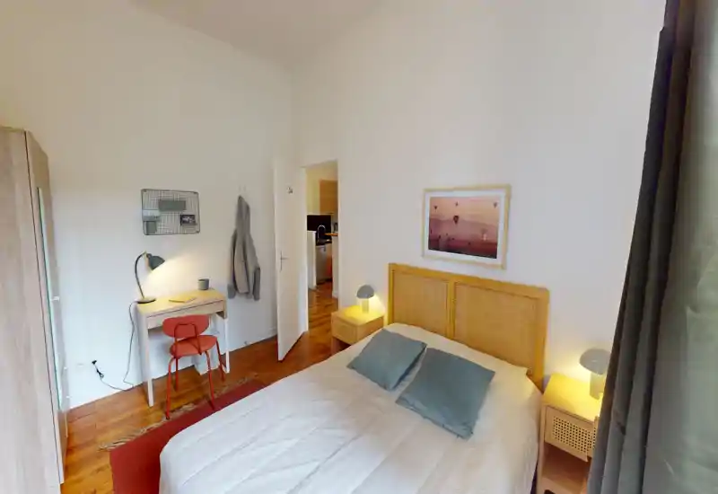 Camera da letto luminosa e curata con letto matrimoniale, comodini con lampade calde; piccolo scrittoio con sedia e armadio visibile.