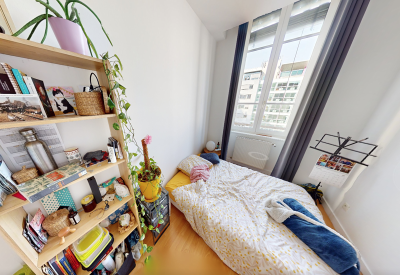 Camera da letto luminosa e accogliente con letto matrimoniale vicino a una grande finestra, scaffali in legno e piante che creano un'atmosfera invitante.