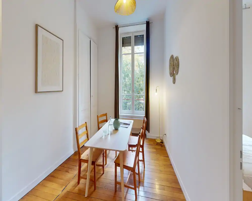 Sala da pranzo stretta con un semplice tavolo in legno e quattro sedie vicino a una finestra alta; il pavimento in legno e la luce naturale soffusa la rendono accogliente per i pasti.