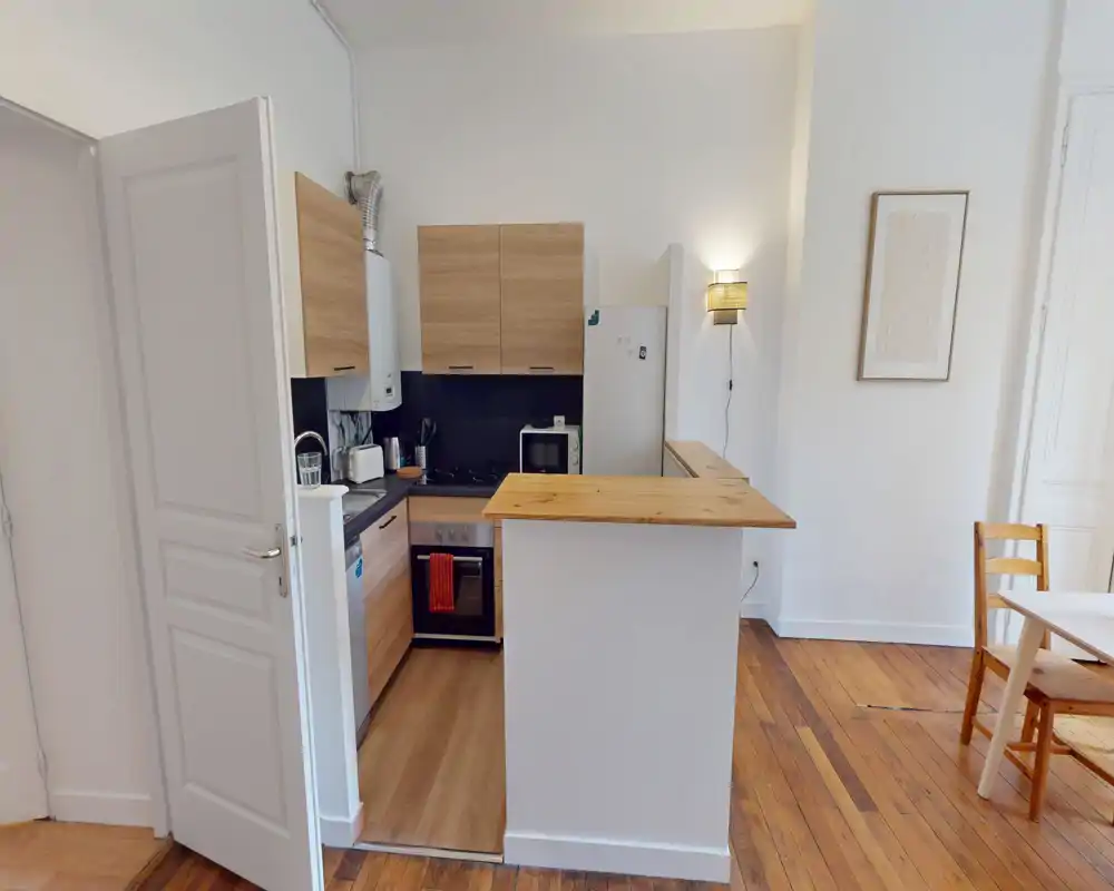 Cucina compatta e moderna con pensili in legno, forno integrato e bancone snack — luminosa, ordinata e ben curata per la vita in città.