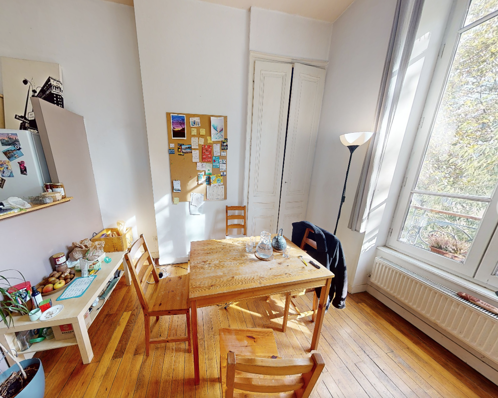 Zona pranzo luminosa con tavolo in legno e quattro sedie accanto a una grande finestra; il pavimento in parquet e gli elementi decorativi semplici creano un ambiente accogliente ideale per i pasti.