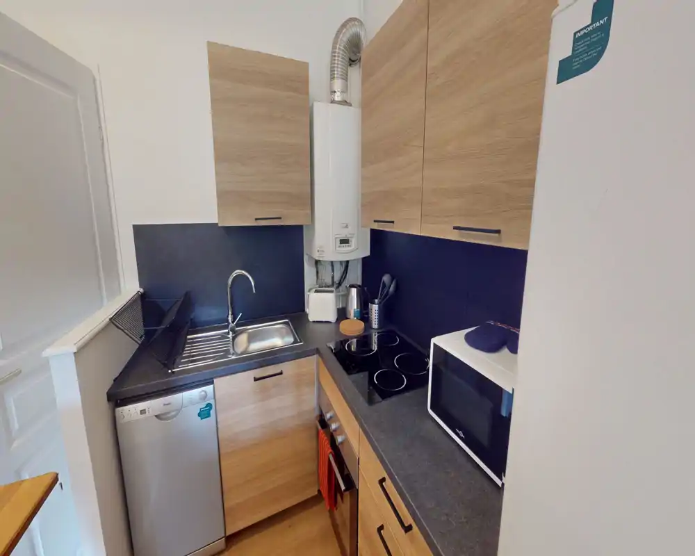 Cucina compatta e moderna con pensili in legno, piano nero, piano a induzione, lavello e elettrodomestici incorporati—ben organizzata per un appartamento piccolo.