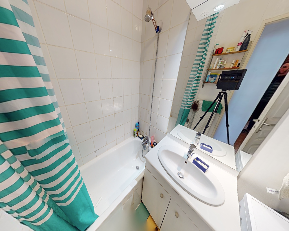 Bagno compatto e ben illuminato con vasca, doccia, lavabo con mobiletto e specchio. Piastrelle bianche e tenda da doccia a righe donano un aspetto pulito e fresco.