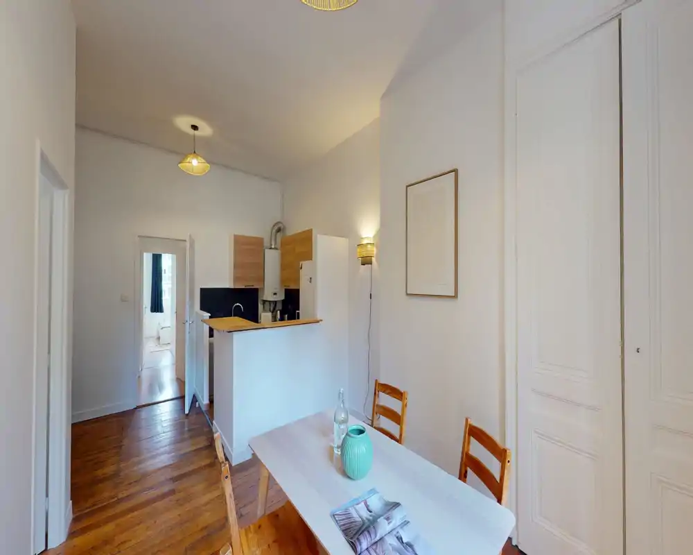 Angolo cottura open-plan luminoso con piccolo tavolo da pranzo e sedie in legno, elettrodomestici compatti e mobili in legno chiaro — perfetto per un appartamento cittadino accogliente.