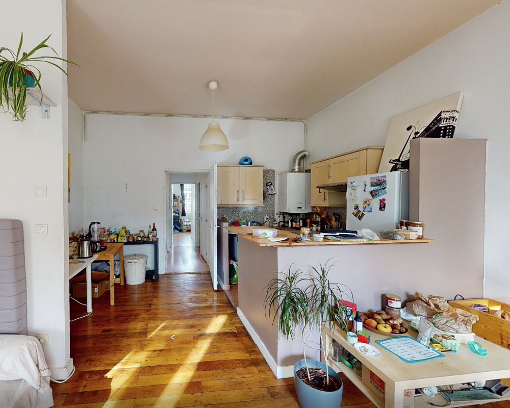 Soggiorno con angolo cottura open space, pavimento in legno, piccolo bancone e pensili della cucina; luce naturale abbondante e arredamento vissuto.