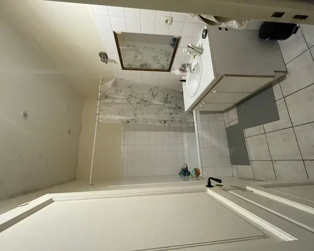 Salle de bains fonctionnelle avec baignoire et rideau de douche, meuble lavabo avec miroir, carrelage au sol et aux murs — compacte et pratique.