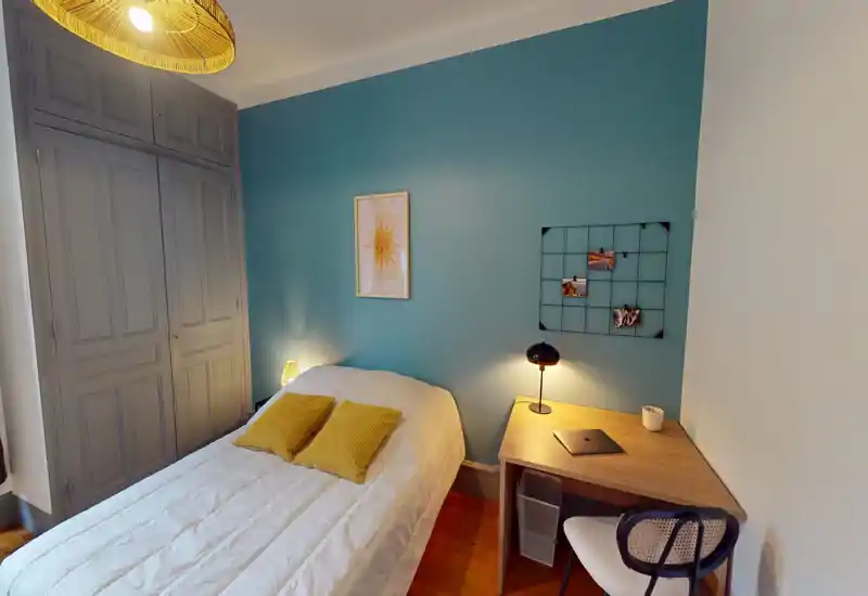 Bright, stylish bedroom with a comfortable double bed against a teal accent wall, bedside lamps and a small wooden desk — ideal for rest and light work.