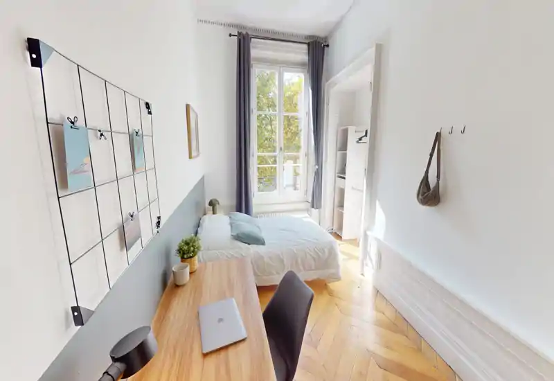 Bright, modern bedroom with a comfortable double bed placed under a large window, a wooden desk and decorative accents creating a calm workspace.