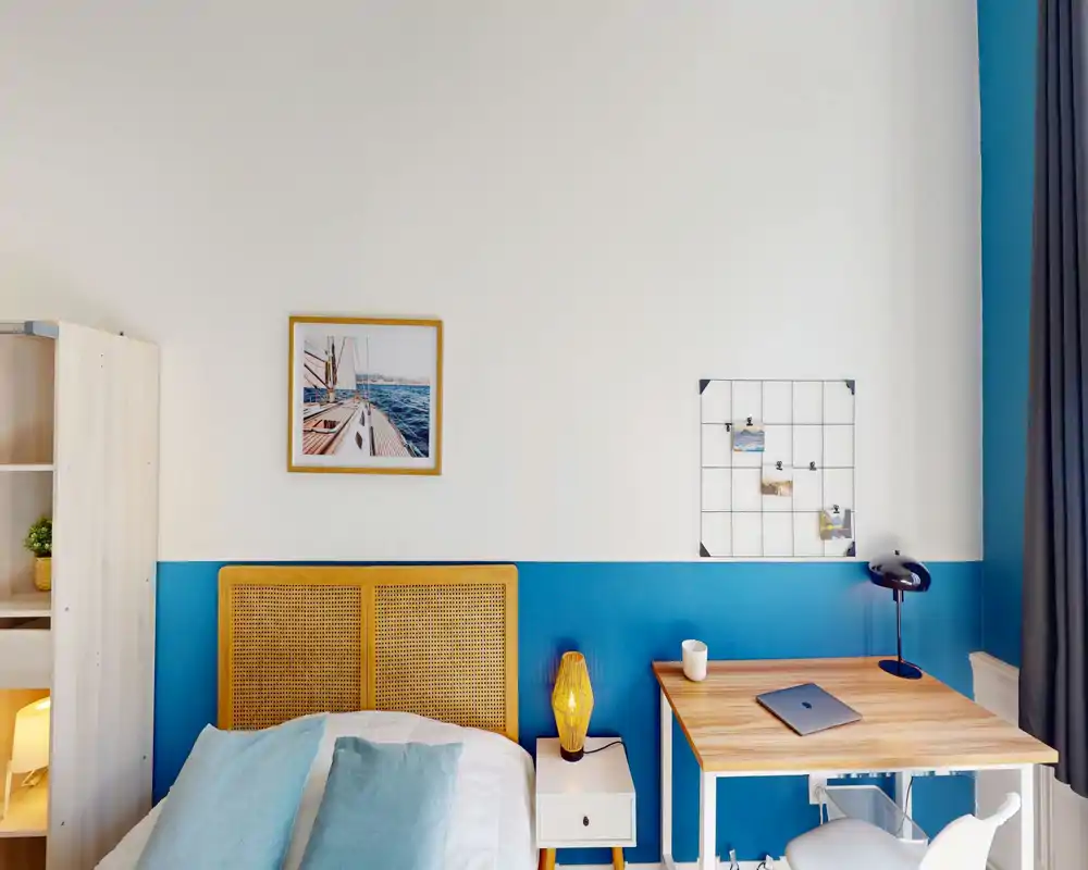 Bright, modern bedroom with a rattan headboard, crisp bedding and a wooden desk by the window — cozy yet minimalist styling ideal for a short-term rental.