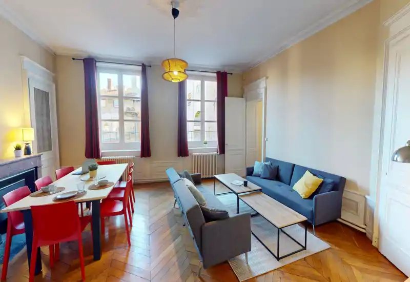 Spacious, stylish living room with a dining area: two comfortable grey sofas, coffee tables, and a six-seat dining table by large windows that fill the space with natural light.