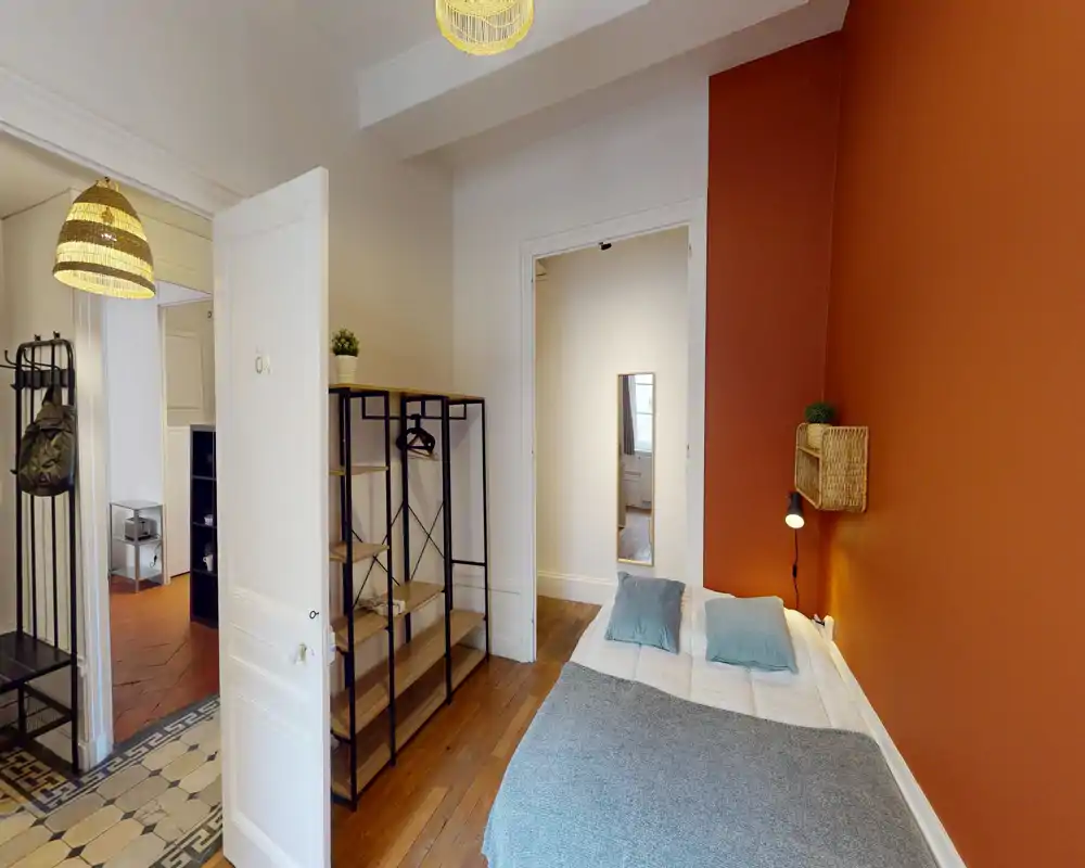 Bright, cozy bedroom with a double bed against a warm terracotta accent wall, bedside lamp and soft textiles; open shelving and wooden floors add a homely, stylish touch.