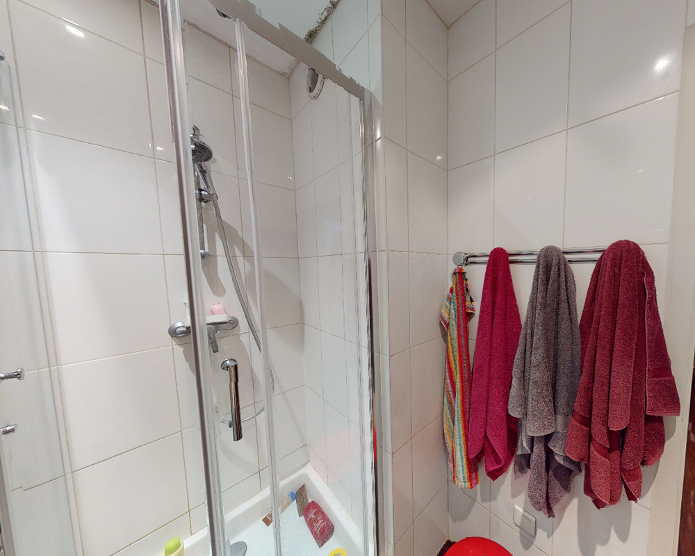 Compact tiled bathroom with a glass-enclosed shower cubicle, chrome fixtures and a towel rack with colorful towels.