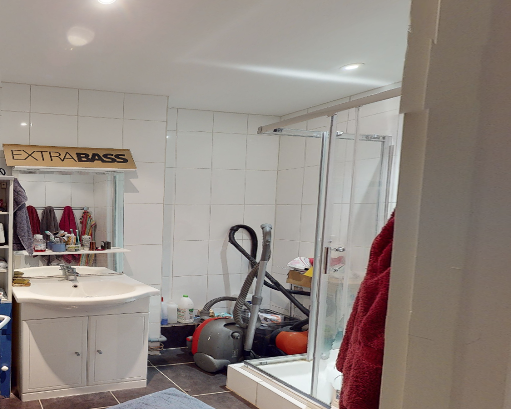 Bathroom with sink, mirror cabinet and a glass shower cubicle; some cleaning equipment and toiletries are visible.