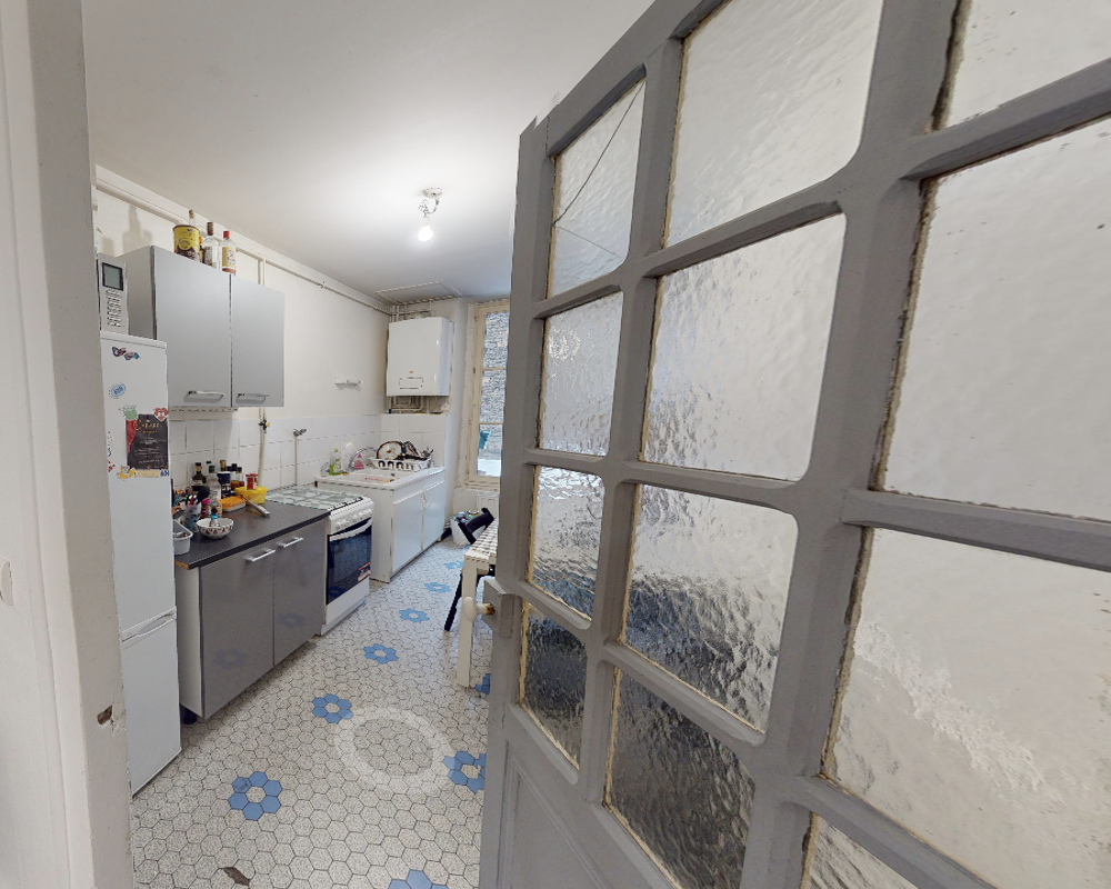 Cuisine compacte et fonctionnelle avec sol carrelé, plaques de cuisson, petits appareils sur le plan de travail et un coin repas près de la fenêtre — lumineuse et pratique pour un usage quotidien.