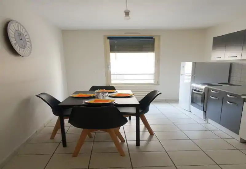 Cucina moderna compatta con tavolo da quattro posti, piano cottura elettrico e frigorifero. Luminoso, minimale e ordinato — ideale per un appartamento in affitto breve in città.