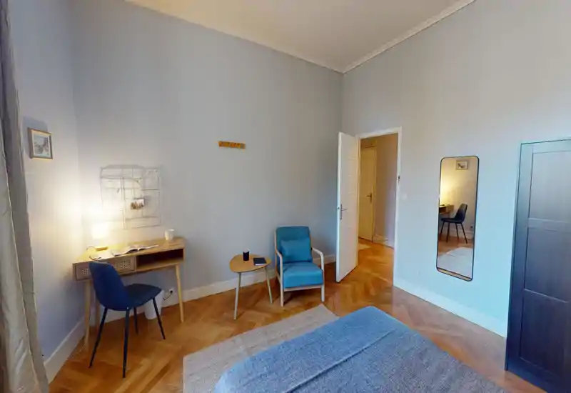 Bright, stylish bedroom with a visible double bed, wooden parquet, a cozy armchair and a small desk — ideal for comfortable stays and remote work.