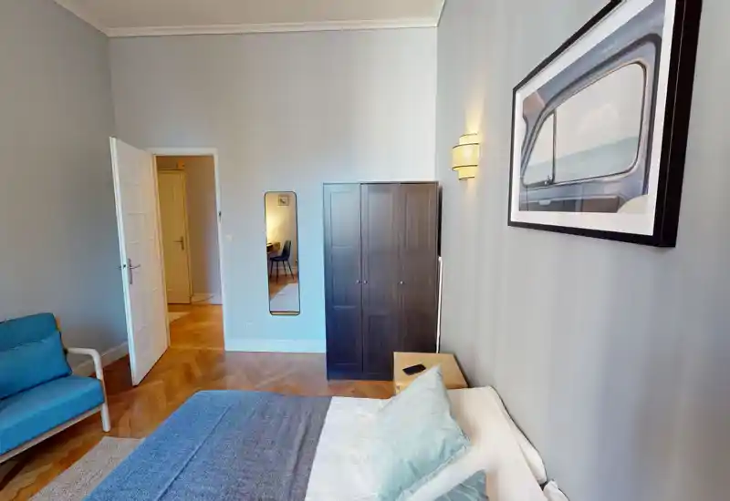 Camera da letto luminosa e curata con letto matrimoniale, comodino e armadio scuro; pavimento in parquet caldo e accenti pastello per un'atmosfera rilassante.