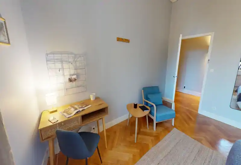Bright, well-staged living area with a small desk, two comfortable chairs and warm parquet flooring — ideal for relaxing or working.