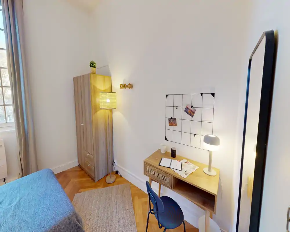 Camera da letto luminosa e accogliente con parquet in legno, una scrivania compatta e lampada da comodino — perfetta per lavoro e relax.