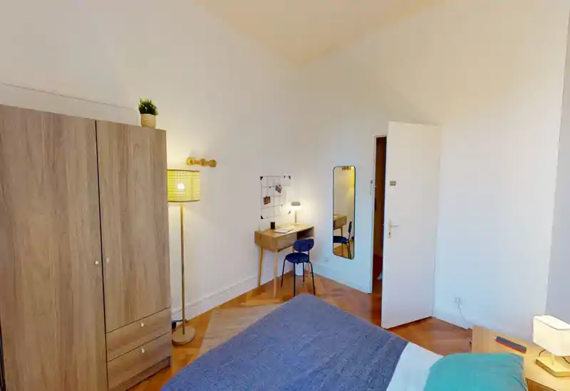 Camera da letto luminosa e ben arredata con letto ben visibile in primo piano, armadio in legno, scrivania e illuminazione calda — accogliente e pronta per gli ospiti.
