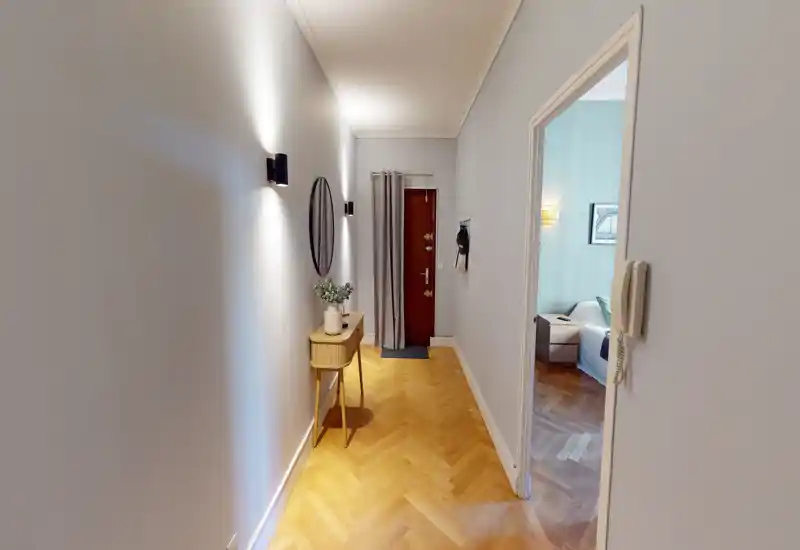 Bright, well-lit entrance hallway with chevron wood flooring, a slim console table with decorative vase and round mirror, and a secure front door — welcoming first impression.