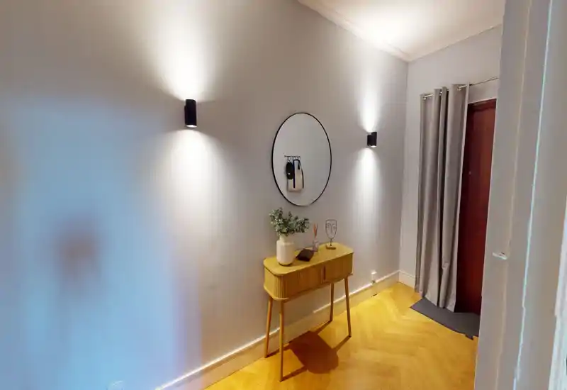 Welcoming entrance hallway with a slim console table, round mirror and soft wall sconces; warm parquet flooring and neutral curtains create a calm first impression.