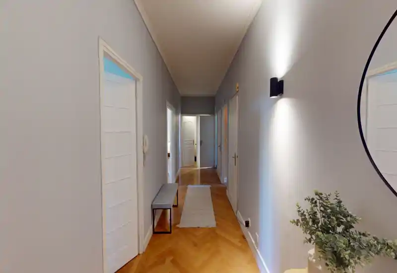 Long, well-lit hallway/entrance with parquet flooring, bench and runner rug — a welcoming corridor leading to interior rooms.