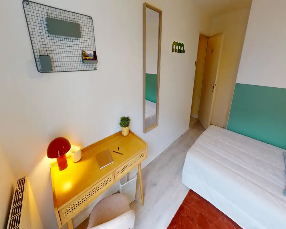 Chambre simple lumineuse et bien décorée avec lit soigné, bureau en bois et lampe chaleureuse — idéale pour un étudiant ou un voyageur seul.