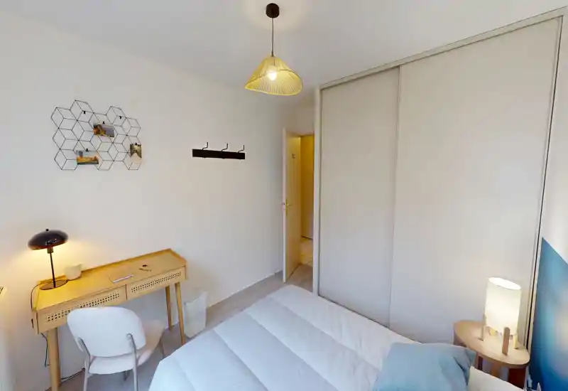Bright, tidy bedroom with a double bed, bedside lamp and built-in sliding wardrobe. A small wooden desk and chair add workspace; neutral tones and soft textiles create a calm atmosphere.
