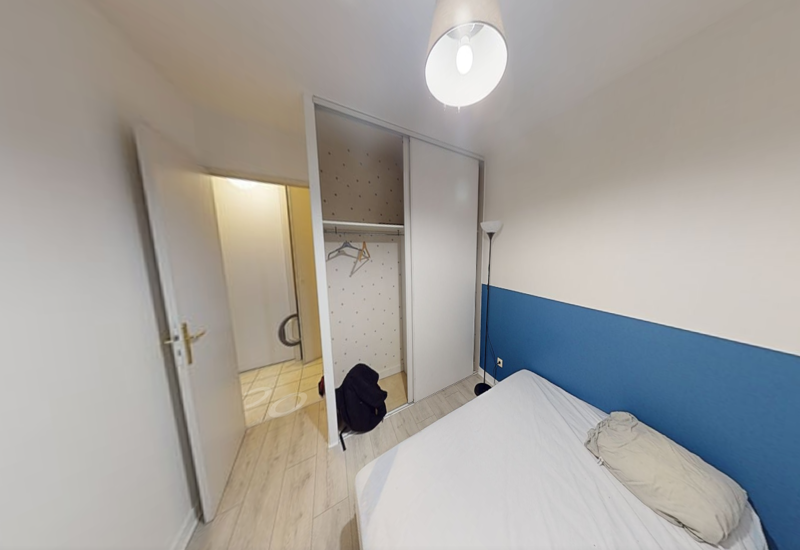 Compact bedroom with a double bed pushed to the right, a built-in sliding-door wardrobe and soft overhead lighting. The blue accent wall and light wood floor create a neat, modern look ideal for a rental listing.