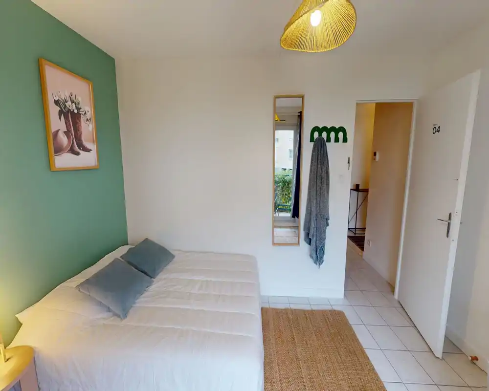 Bright, neatly styled bedroom with a double bed, soft pillows, a decorative rug and a full-length mirror near the entrance — ideal for a cozy short-stay.