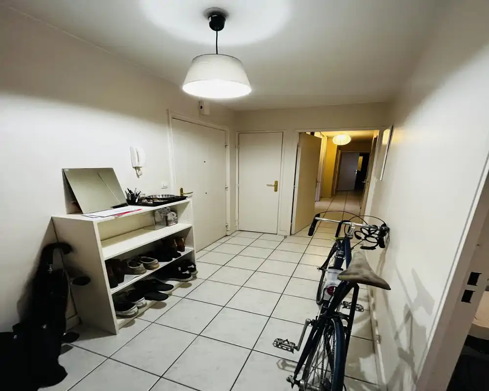 Hall d'entrée carrelé et lumineux avec une étagère à chaussures, une suspension et un vélo appuyé contre le mur — espace d'arrivée fonctionnel.