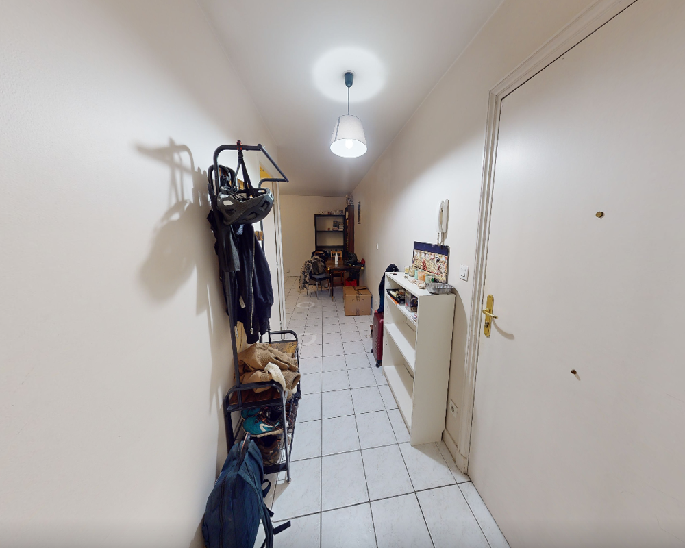 Entrée/couloir étroit avec sol carrelé, porte-manteau mural et rangement à chaussures ; suspension lumineuse et étagères près de la porte d'entrée.