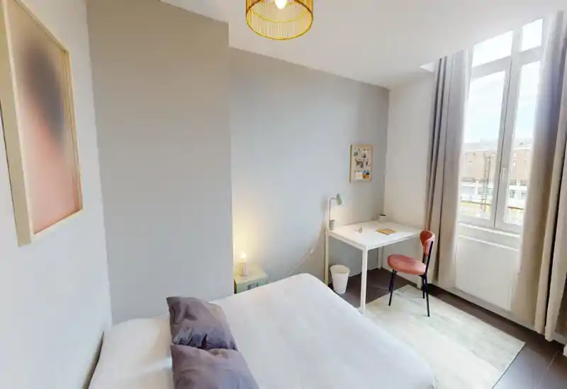 Bright, modern bedroom with a double bed, soft pillows and a small workspace by a large window letting in plenty of natural light.