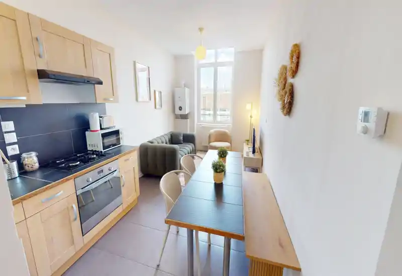 Pièce de vie claire et compacte avec petite cuisine équipée, table à manger et coin salon cosy près de la fenêtre — idéal pour un studio citadin.