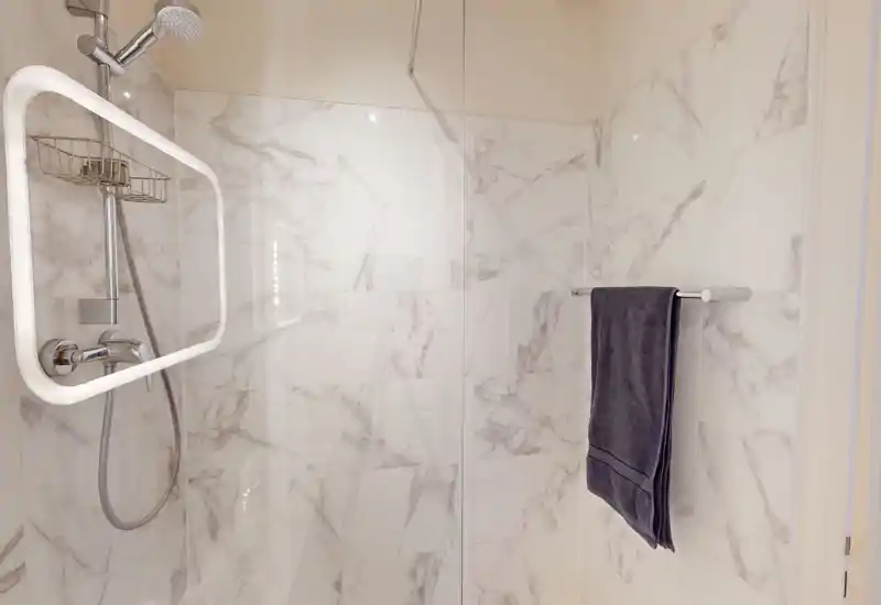 Salle de bain moderne avec carrelage effet marbre, cloison en verre et robinetterie chromée ; une serviette est accrochée à la barre.