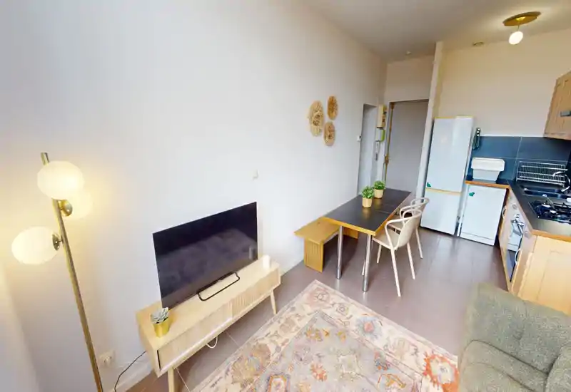 Espace séjour lumineux et chaleureux avec une configuration ouverte et compacte comprenant un meuble TV, une table à manger et une kitchenette visible — idéal pour un petit appartement.