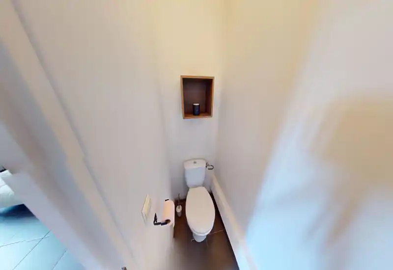 WC compact avec toilette, niche murale pour rangement et murs blancs neutres — petit espace sanitaire lumineux et fonctionnel.