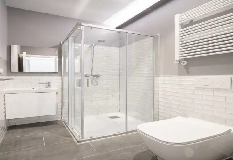 Bagno moderno e luminoso con doccia in vetro, WC sospeso e mobile lavabo a parete. Piastrelle bianche e pavimento grigio neutro per un aspetto contemporaneo.