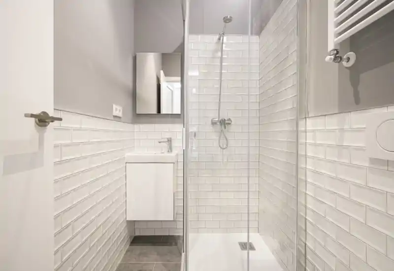 Bagno moderno e compatto con cabina doccia in vetro, piastrelle bianche effetto metro e piccolo lavabo a parete con specchio.