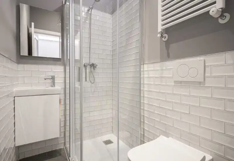 Bagno moderno e compatto con cabina doccia in vetro, wc sospeso e piccolo lavabo con specchio. Piastrelle bianche effetto metro e tonalità neutre regalano un aspetto pulito e contemporaneo.
