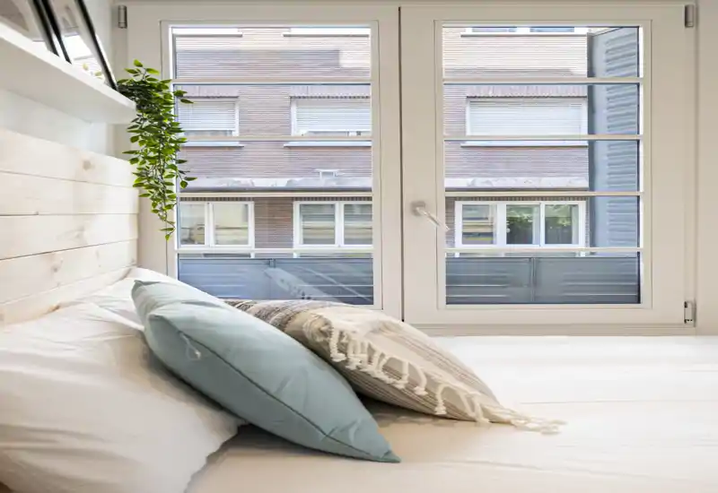 Angolo camera da letto luminoso e accogliente con cuscini decorativi e ampia finestra che garantisce luce naturale — perfetto per foto annuncio che valorizzano comfort e luce.