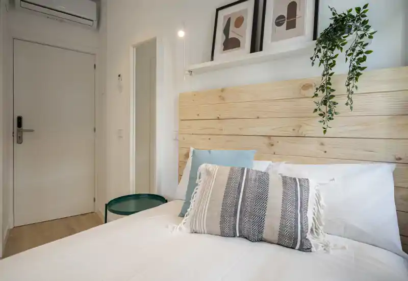 Camera da letto luminosa e ben arredata con testiera in legno, cuscini decorativi e biancheria neutra: ideale per foto di annunci che comunicano comfort e stile.