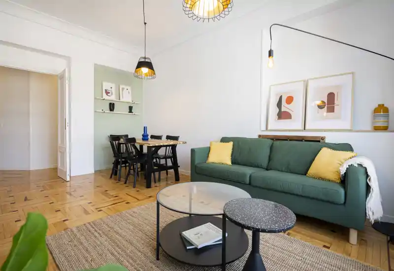 Sala luminosa y bien decorada con sofá verde, cojines decorativos, mesas de centro redondas y zona de comedor — espacio moderno y acogedor, ideal para descansar y recibir invitados.