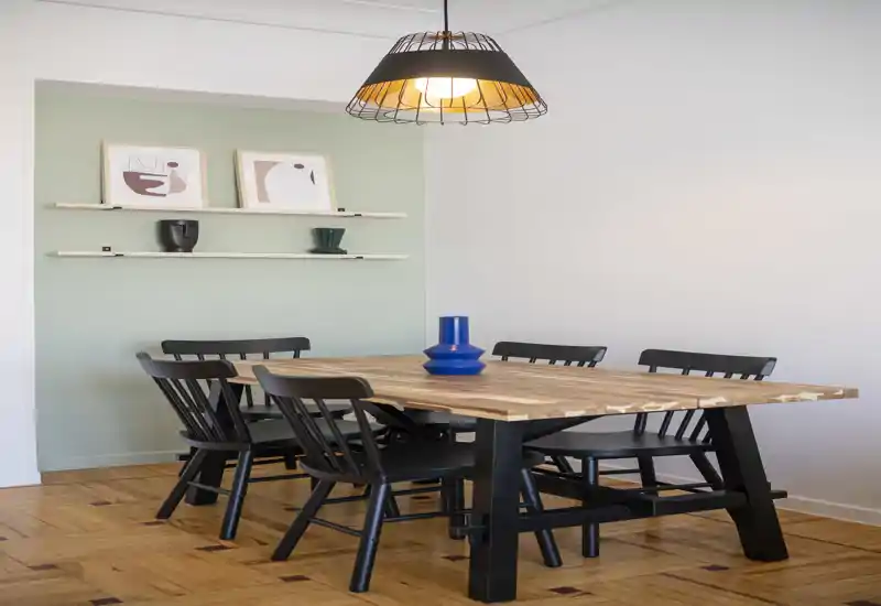 Comedor con estilo, mesa grande de madera, sillas negras y lámpara colgante cálida — perfecto para comidas y reuniones.