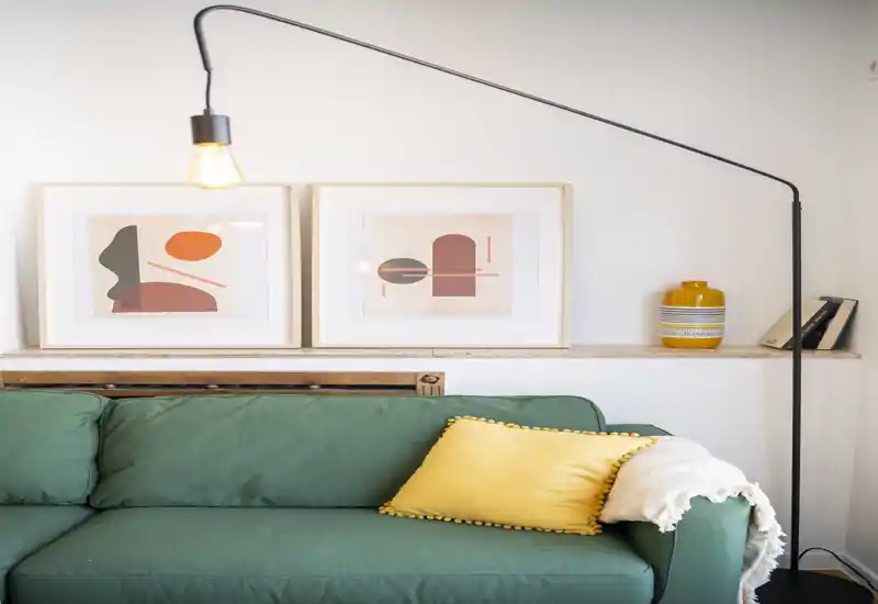 Sala luminosa y con estilo con sofá verde, cojín amarillo y lámpara de pie moderna: perfecta para relajarse en un espacio acogedor y bien decorado.
