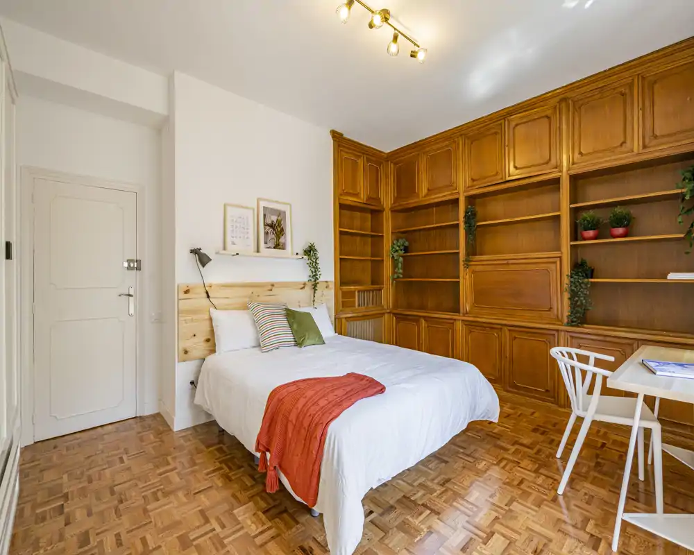 Bright, cozy bedroom featuring a double bed with wooden headboard, large built-in wooden shelving, parquet floor and a small desk — ideal for a comfortable stay or a work-from-home night.