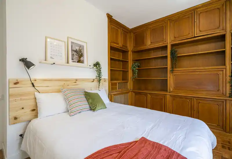 Bright, stylish bedroom with a large comfortable bed, decorative cushions and warm built-in wooden shelving creating a cozy atmosphere.