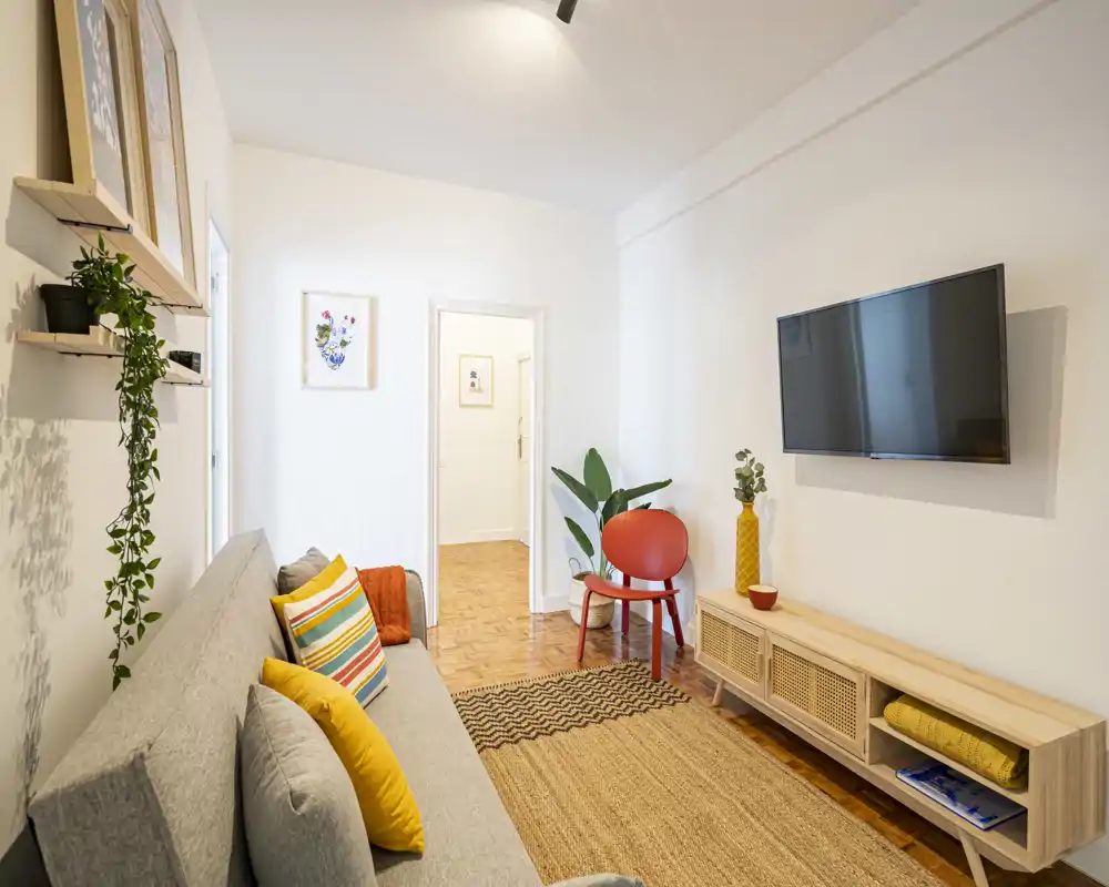 Bright, stylish living room with a comfortable sofa, colorful cushions, natural textures and a wall-mounted TV — ideal for relaxing.