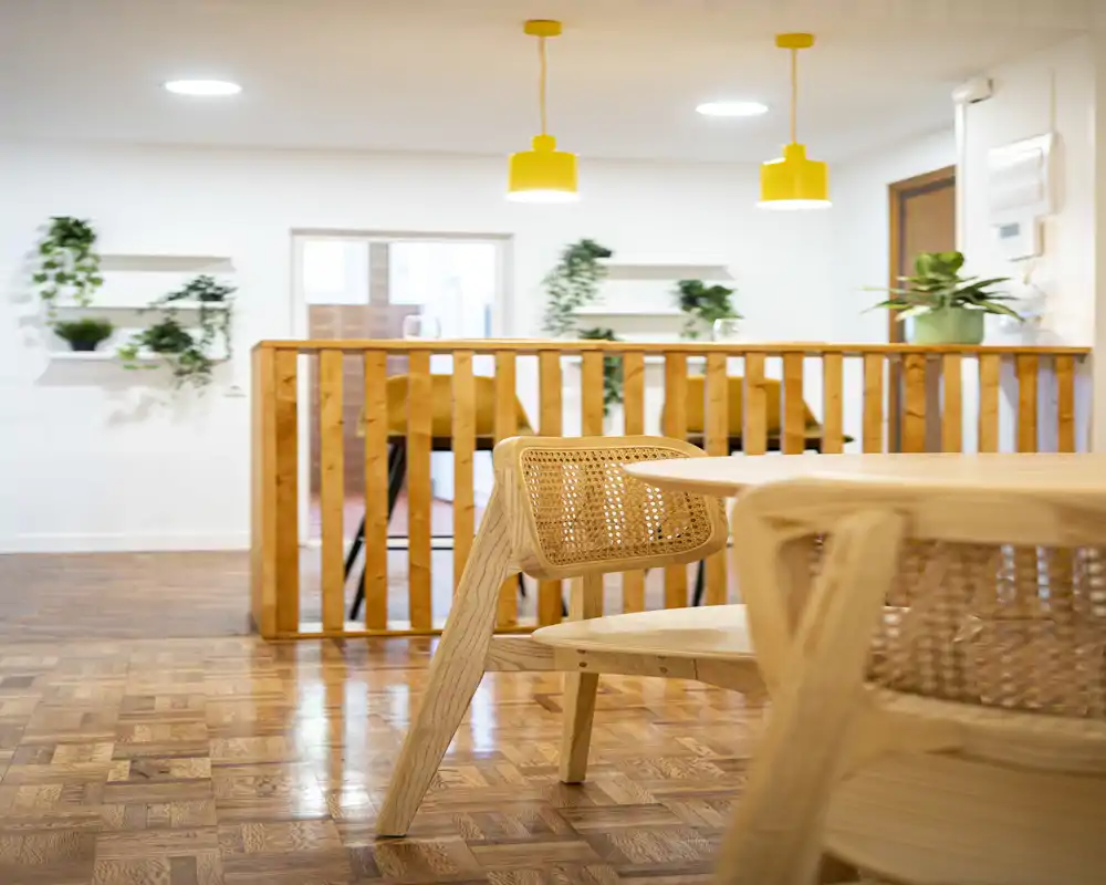 Bright, cozy dining area with light wooden table and woven chairs, warm pendant lights and indoor plants creating a welcoming atmosphere.